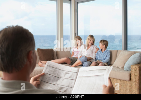 Madre e bambini seduti sul divano di casa vacanze vicino al mare, padre quotidiano di lettura Foto Stock