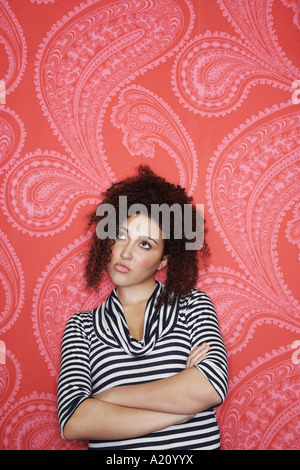 Ragazza adolescente in piedi con le braccia incrociate, guardando lontano, di fronte a uno sfondo colorato Foto Stock