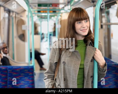 Sorridente, giovane donna in piedi sul treno dei pendolari, barra di contenimento Foto Stock