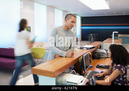 Uomo in piedi presso la reception, parlando a receptionist Foto Stock