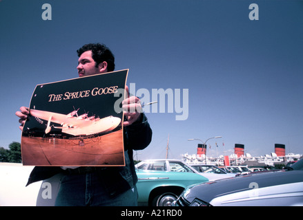 L uomo può contenere fino poster di Howard Hughes' piano ' Spruce Goose' in un parcheggio auto con tre imbuti di Queen Mary dietro Foto Stock