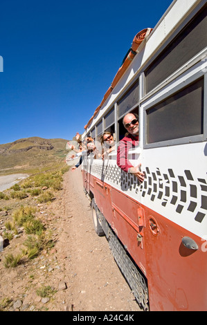 Un overland adventure holiday carrello che viaggia lungo una strada sterrata in Perù con i passeggeri appoggiata dalla finestra sventolando. Foto Stock