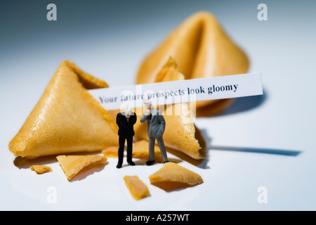 Due imprenditore in miniatura nella parte anteriore del Fortune cookie con la lettura del messaggio del vostro futuro propsects sguardo malinconico Foto Stock