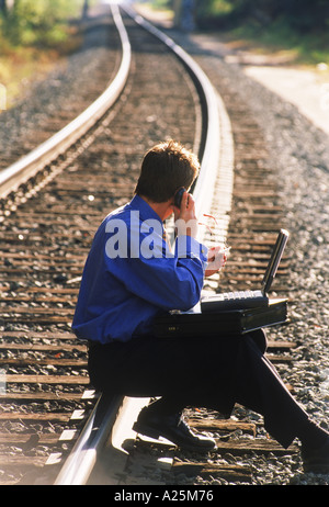 Imprenditore con laptop e cellulare seduti sulla ferrovia via Foto Stock
