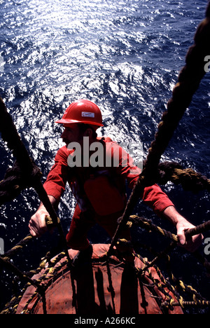 Un lavoratore nel commercio di olio di sguardi oltre l'orizzonte come egli esegue le riparazioni sospesa in alto al di sopra di un off shore rig. Foto Stock