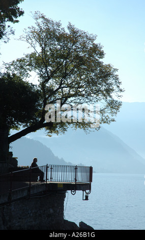 Un vecchio uomo seduto in ombra di alberi che si affaccia sul lago di como Foto Stock