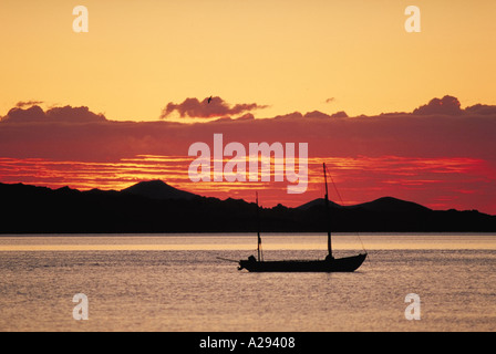 Una barca a vela è ormeggiata in acque della Baja California Messico con montagne stagliano sullo sfondo contro un tramonto rosso Foto Stock
