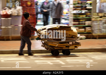 La donna spinge un carrello impilato con cartone riciclato, Hong Kong, Cina Foto Stock