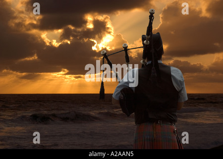 Un lone bagpiper svolge la sua canzone luttuoso nella parte anteriore di un bellissimo tramonto sull'oceano. Foto Stock