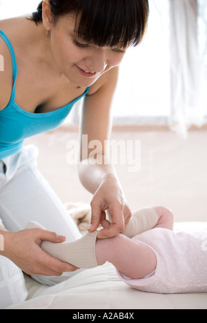 Madre messa calze su bambinos piedi Foto Stock