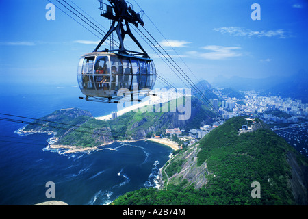 Funivia caricato con passeggeri approssimarsi al top del pan di zucchero o Pao de Acucar con le coste di Rio de Janeiro al di sotto di Foto Stock