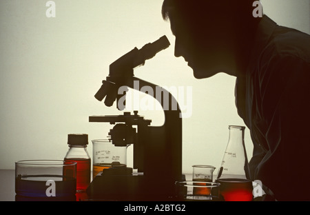 Silhouette di scienziato maschio in lab guardando attraverso il microscopio Foto Stock