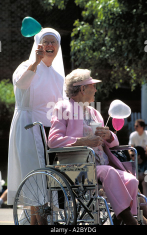 Nun tenendo un palloncino spingendo una donna anziana in una sedia a rotelle in una parata. San Paolo, Minnesota Foto Stock