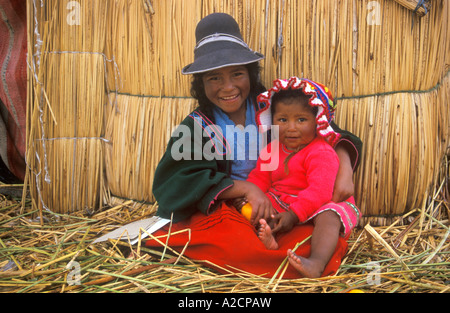 Tradizionalmente vestiti bambini seduti accanto a una capanna di paglia su un Uro Isola una delle numerose isole galleggianti nel Lago Titicaca Foto Stock