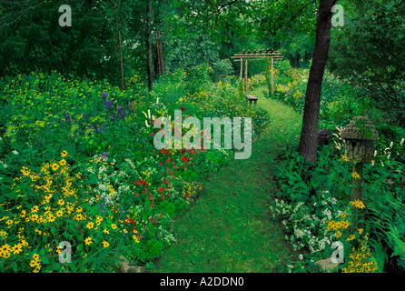Percorso in giardino naturale in erba falciata che conduce a un'arcata in legno attraverso un giardino privato all'ombra di alberi autoctoni nel cortile posteriore del Missouri, Stati Uniti Foto Stock