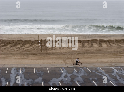 Ciclista pedala sul percorso vicino alla sabbia temporanea berm che protegge le spiagge da sopra la media di onde alte Foto Stock