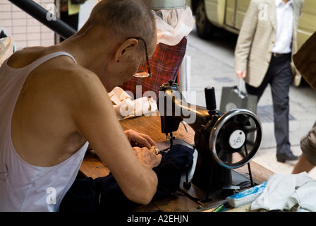 Dh Pottinger Street CENTRAL HONG KONG vecchio uomo cinese rammendo vestiti con cucitura a macchina worker manodopera in Cina Foto Stock