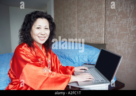 Ritratto di una donna matura utilizzando un laptop sorridente in camera da letto Foto Stock