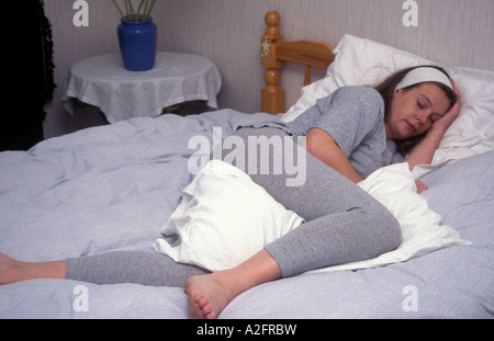 Fortemente incinta adolescente/giovane donna disteso in appoggio sul letto in posizione comoda, cuscini sotto bump Foto Stock