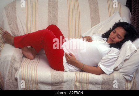 Incinta donna ispanica sdraiato a riposare sul divano Foto Stock