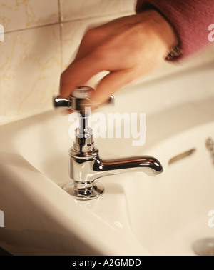 Una mano di donna si spegne l'acqua che scorre da un bagno di cromo tocca Foto Stock