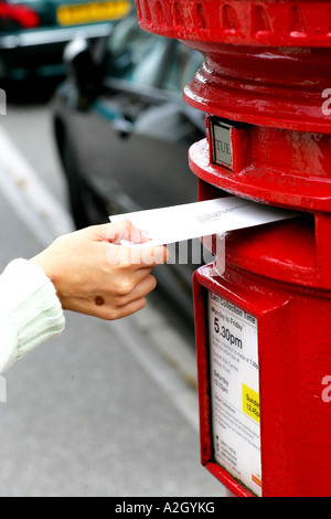 Persona che pongono una lettera in un rosso Post Office inviare casella sul lato di una strada Foto Stock