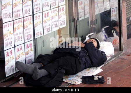 Senzatetto uomo dorme nella parte anteriore di costosi immobili business, la Causeway Bay di Hong Kong Foto Stock