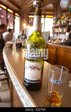 Una bottiglia di Ricard 45 pastis e un vetro su una barra di zinco in un cafe bar di Parigi. Sullo sfondo la gente seduta al bar a e b Foto Stock