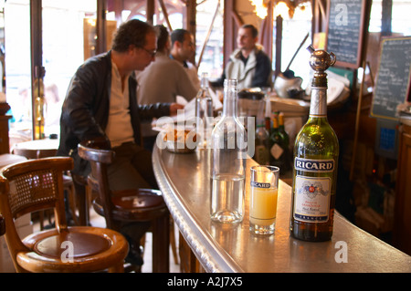 Una bottiglia di Ricard 45 pastis e un bicchiere e una caraffa di acqua su una barra di zinco in un cafe bar di Parigi. Sullo sfondo la gente si Foto Stock