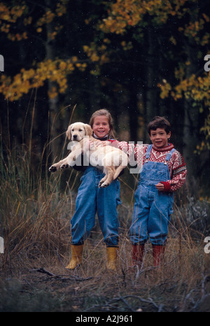 Sorridenti un ragazzo e una ragazza in piedi fuori in una flurrying giornata autunnale la ragazza detiene un golden retriever cucciolo nelle sue braccia Foto Stock