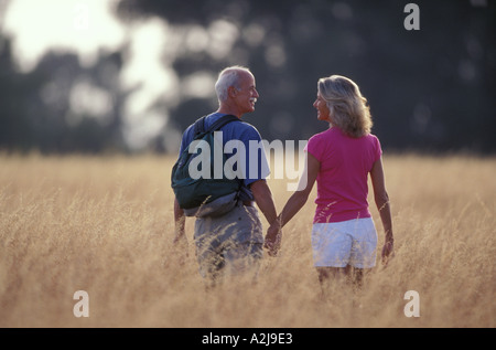 Casualmente vestito coppia matura il sorriso a vicenda come camminano mano nella mano attraverso hip alta erba gialla Foto Stock