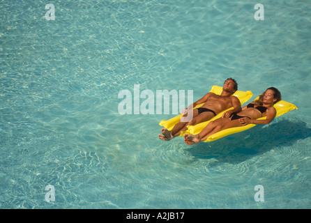 Giovane floating fianco a fianco su giallo zattere gonfiabili in una grande piscina Foto Stock