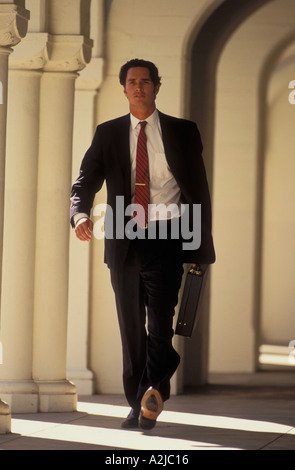 Interessato alla ricerca imprenditore porta una valigetta come egli cammina lungo un portico colonnato Foto Stock