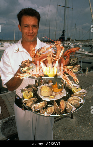 L'Europa, Francia, Ile de Re, Ars en Re. Cameriere piastra portante di piatti a base di frutti di mare Foto Stock