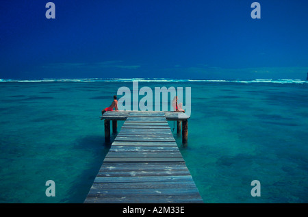 Vista guardando verso il basso ocean pier nei tropici di un uomo e di una donna che indossa red costume da seduto su lati opposti del molo Foto Stock