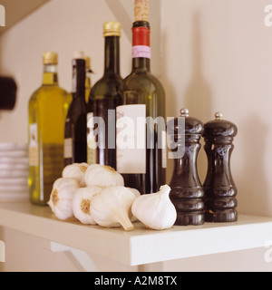 Scaffale con bottiglie di vino, olio e aceto insieme con spicchi di aglio e sale e pepe mills Foto Stock