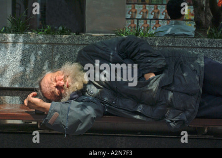 Senzatetto uomo dorme sul banco in New York City Foto Stock