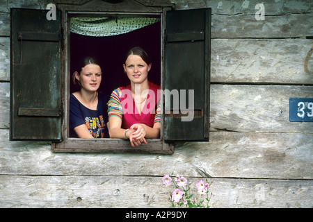 Due giovani ragazze guardando fuori da una finestra di una capanna in legno, Croazia Foto Stock