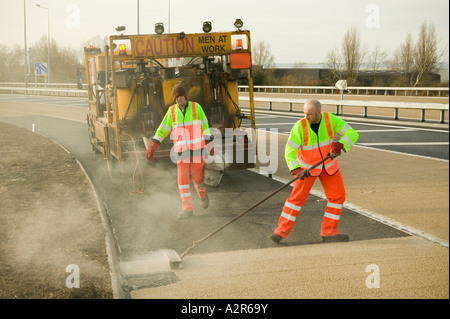 Lavoratori edili posa di superficie antislittamento alla superficie di una nuova strada Foto Stock