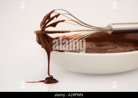In acciaio inox frusta sul lato della vaschetta di colore bianco con il mix di cioccolato sfondo bianco Studio shot Foto Stock