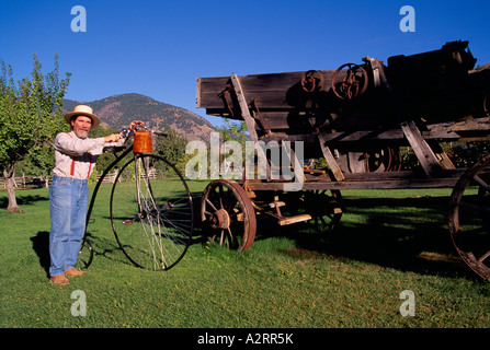 Keremeos, BC, Similkameen Valley, British Columbia, Canada - Uomo con Penny Farthing accanto al vecchio carro a Grist Mill e giardini Foto Stock