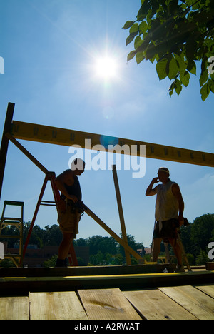 Silhouette di due lavoratori edili sulla parte superiore del tetto della casa sul caldo giorno d'estate Foto Stock