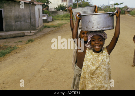 Mozambico Quelimane giovani sorridenti bambini che portano vasche in metallo pentole benne sulle loro teste Foto Stock