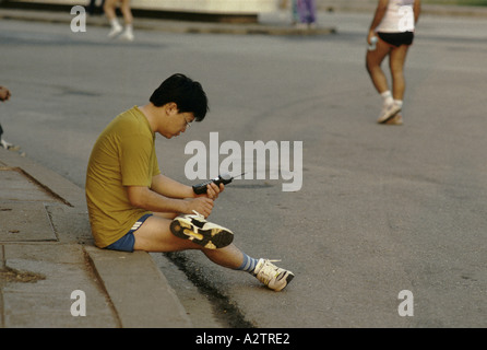 Pareggiatore avente una pausa seduta sul marciapiede in Bangkok, utilizzando il suo telefono cellulare, Thailandia Foto Stock