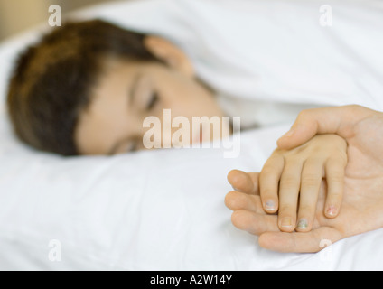 Bambino giacente in letto, mano del padre di contenimento del bambino Foto Stock