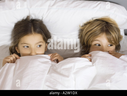Due bambini che giace nel letto con coperchio tirato fino a naso Foto Stock