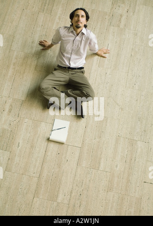 Uomo seduto sul pavimento con imbottitura di carta davanti a lui Pendente ritornare, ad alto angolo di visione Foto Stock