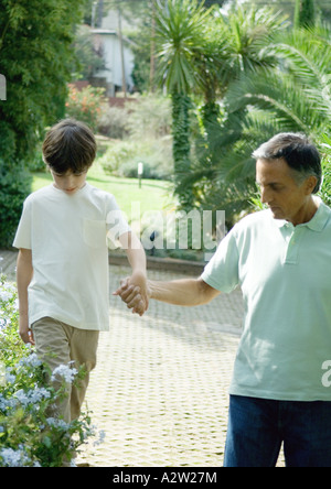 Uomo maturo holding ragazzi mano come egli cammina sulla mensola Foto Stock