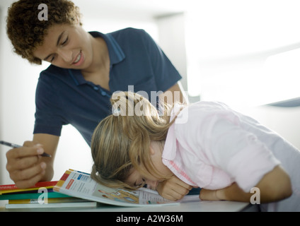 Ragazzo adolescente aiutando la sorella con i compiti, la ragazza a testa in giù sui libri Foto Stock