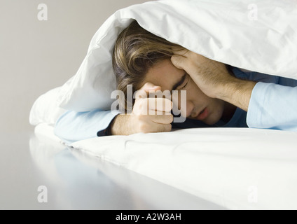 Uomo disteso sotto i coperchi, tenendo la testa Foto Stock